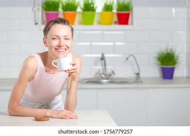 Balance in life concept. Beautiful woman drinking tea in white kitchen with green wheatgrass for juice on the background - Powered by Shutterstock