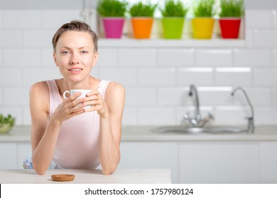 Balance in life concept. Beautiful woman drinking tea in white kitchen with green wheatgrass for juice on the background - Powered by Shutterstock