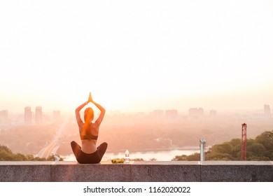 Balance With Nature And The City. Rear View Of Young Beautiful Fit Woman In Sportswear Doing Yoga While Sitting Against Industrial City View
