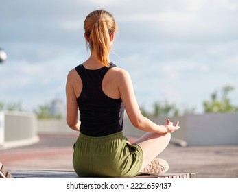 Balance With Nature And The City. Rear View Of Young Beautiful Fit Woman In Sportswear Doing Yoga While Sitting And Meditating In City Park In Sunny Summer Day.