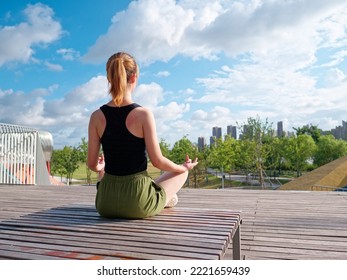 Balance With Nature And The City. Rear View Of Young Beautiful Fit Woman In Sportswear Doing Yoga While Sitting And Meditating In City Park In Sunny Summer Day.