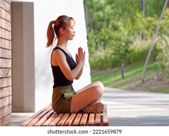 Balance With Nature And The City. Side View Of Young Beautiful Fit Woman In Sportswear Doing Yoga While Sitting And Meditating In City Park In Sunny Summer Day.