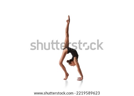Balance. Portrait of junior gymnast in black sport swimsuit doing gymnastics excercises isolated over white background. Sport, skills, achievements. Grace of cat
