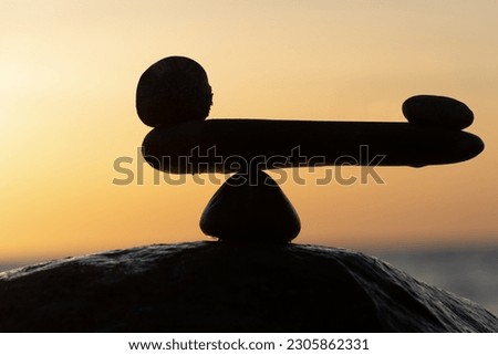 in the balance of power - natural scales of stones by the sea to the orange sunset - symbol photo	
