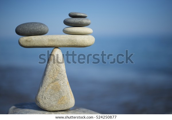 Balance of stones. To weight pros and\
cons. Balancing stones on the top of boulder. Close up. Balance of\
stones on a blue sky background with a copy space. Scales. Stones\
balance,\
sustainability.