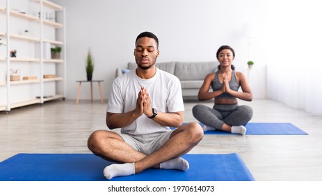 Balanced Black Guy Meditating With Closed Eyes, Sitting In Lotus Pose, Doing Namaste Gesture, Practicing Yoga With His Girlfriend At Home, Panorama. Reaching Inner Peace And Mindfulness