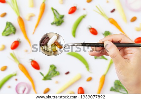 Balanced healthy vegan, plant based supplements concept. Top view close up of a spoon full of Vitamins and protein capsules with colorful phytonutrients vegetables as a background. Multivitamins, B12