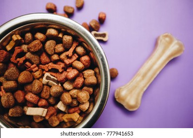 Balanced meal for a pet. A bowl of dry dog food and a dog chew bone on a bright one-color purplebackground, top view. Pet care and veterinary concept. Spase for your text or image.