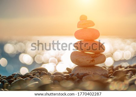 Balanced Pebbles Pyramid on the Beach on Sunny Day and Clear Sky at Sunset. Blue Sea on Background Selective focus, zen stones on sea beach, meditation, spa, harmony, calm, balance concept