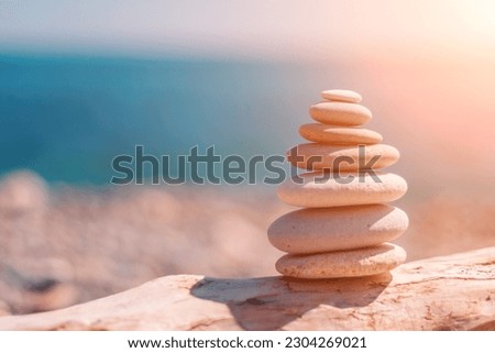 Balanced rock pyramid on sea pebbles beach, sunny day and clear sky at sunset. Golden sea bokeh on background. Selective focus, zen stones on sea beach, meditation, spa, harmony, calm, balance concept