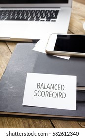 Balanced Scorecard Text On Business Card At Desktop In Office With Laptop, Tablet Computer And Phone.