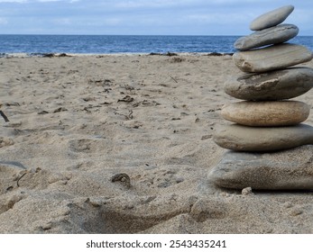 A balanced stack of smooth stones carefully arranged on a sandy beach by the ocean. This serene coastal scene invites thoughts of mindfulness, relaxation, and the calming rhythm of the sea waves. - Powered by Shutterstock