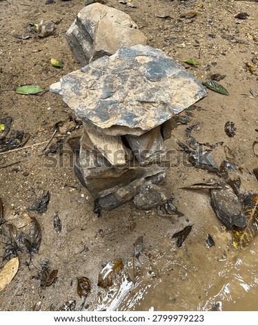 A balanced stone stack, or cairn, carefully constructed on the wet, sandy ground near a riverbank, showcasing a moment of peace, zen, and natural artistic arrangement in the wild outdoors.

