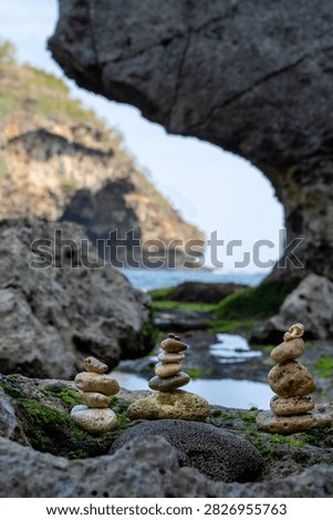 Balanced stone stack on a mossy rocky beach with natural rock arch and ocean cliff background
