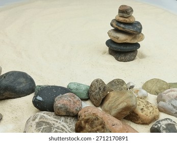 Balanced zen stone tower standing on fine white sand surrounded by assorted natural pebbles. Calm and minimalistic spa inspired composition with earthy tones and a peaceful atmosphere. Perfect for wel