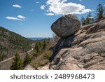 Balancing Bubble Rock in Acadia National Park A large, smooth, gray boulder rests precariously on a rock formation, overlooking a valley with a winding road and a distant view of the ocean.