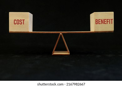 Balancing Cost And Benefit Word On Seesaw Scale In Dark Black Background. Cost-benefit Ratio Business Concept.