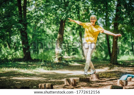 Balancing exercise outdoors. Mature woman standing on one leg, exercising balance 