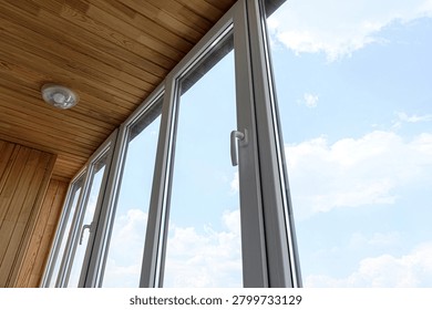 balcony features white-framed plastic windows with sleek handles. ceiling is lined with warm wooden planks and fitted with simple recessed light fixture