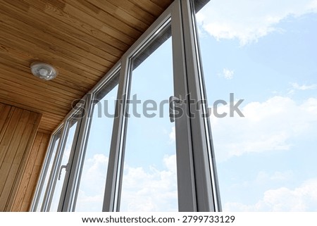 balcony features white-framed plastic windows with sleek handles. ceiling is lined with warm wooden planks and fitted with simple recessed light fixture