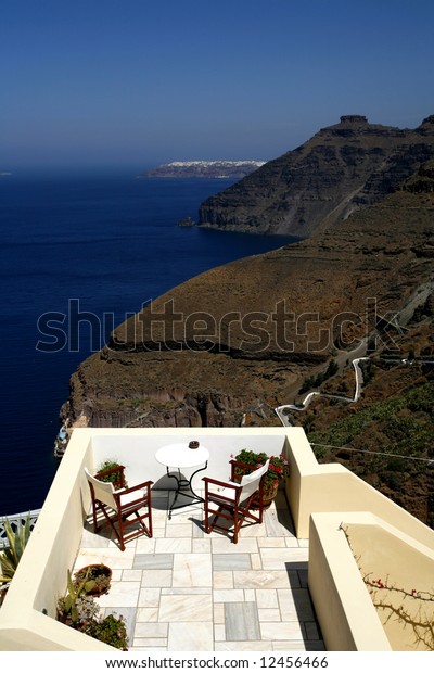 A balcony in Fira,\
Santorini, with a view of the dark volcanic cliffs, the steps to\
the harbour, the cable car and the sea in the caldera of the\
Cycladic island.
