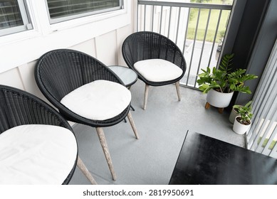 balcony setup with three black wicker chairs, white cushions, a small glass-top table, and potted plants including Zamioculcas zamiifolia, creating a relaxing modern outdoor living space