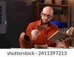 Bald archaeologist in glasses studying an ancient artifact reading a book working late in the office. Copy space
