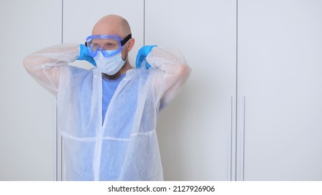 A Bald Bearded Man In A Locker Room Puts On Gloves, A Mask And Glasses Before Visiting An Infected Patient. The Work Of A Nurse In A Covid Hospital During The Outbreak Of Coronovirus Infection