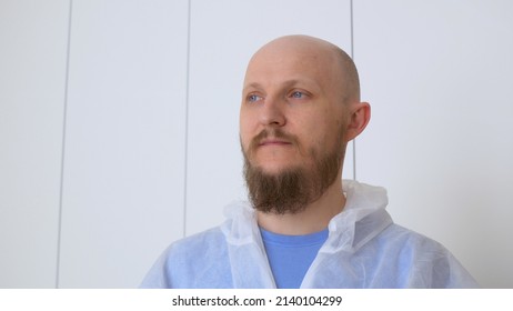 A Bald Bearded Man In A Locker Room In A Protective Suit To Visit The Place Of Origin Of The Coronavirus. The Work Of A Nurse In A Covid Hospital During The Outbreak Of Coronovirus Infection