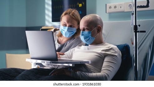 Bald Cancer Patient In Mask And Wife Speaking With Relatives On Laptop In Modern Ward Of Oncology Hospital During Pandemic