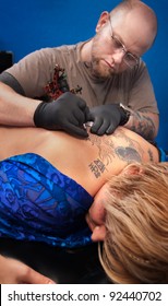 Bald Caucasian Tattoo Artist Creates A Design On Client's Back