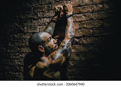 A Bald Gang Member In Tattoos Stands Facing The Wall With His Hands Up In Handcuffs. Arrest Of A Dangerous Criminal. Punishment For A Crime.