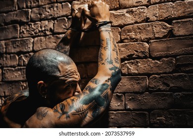 A Bald Gang Member In Tattoos Stands Facing The Wall With His Hands Up In Handcuffs. Arrest Of A Dangerous Criminal. Punishment For A Crime.