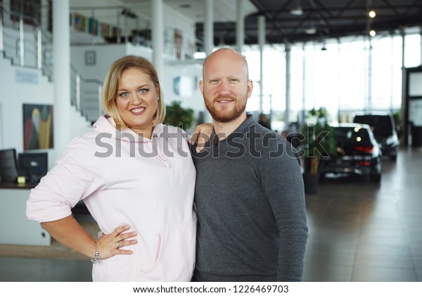 Bald guy and a fat blonde\
woman in a dealership bought a car. The concept of buying a\
vehicle.