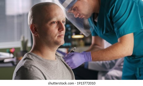 Bald Male Patient With Cancer Talking With Mature Doctor While Assistant Making Coronavirus Vaccine Injection In Hospital