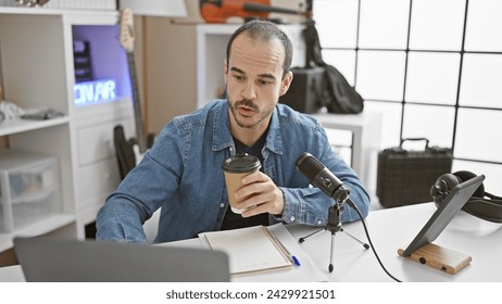 A bald man with a beard in a denim jacket speaking into a microphone during a podcast recording session indoors - Powered by Shutterstock