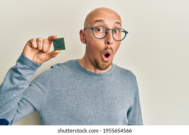 Bald Man With Beard Holding Cpu Computer Processor Scared And Amazed With Open Mouth For Surprise, Disbelief Face 