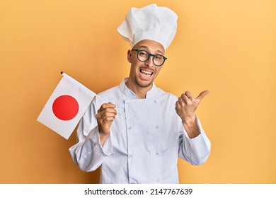 Bald Man With Beard Wearing Professional Cook Uniform Holding Japan Flag Pointing Thumb Up To The Side Smiling Happy With Open Mouth 