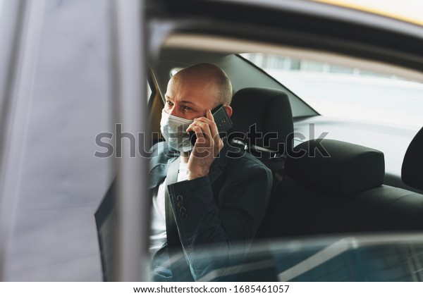 Bald\
man businessman in medical face mask using mobile phone inside\
yellow car taxi. Concept of coronavirus\
quarantine