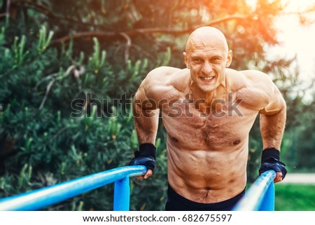 Bald Man doing push ups on parallel bars in a park