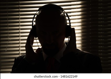 Bald Man With Headphones On The Background Of Closed Blinds, Contour Lighting, Listening To Music On Old Equipment