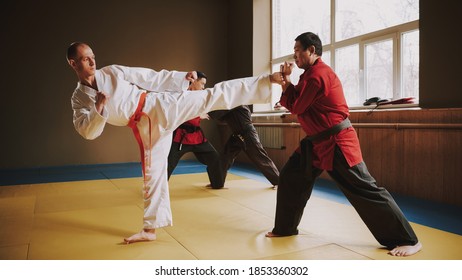 Bald man kicks his opponent in the karate hall. A man in a red kimono and a black belt blocks a kick from a man.  - Powered by Shutterstock