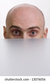 A Bald Man Is Peering Over A Wall With His Brow Furrowed.