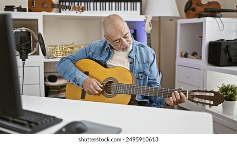 Bald man playing guitar in home office with musical instruments and computer - Powered by Shutterstock