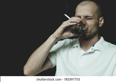 Bald man in white shirt drinking alcohol drink from the glass and smoking cigarette with black background not isolated