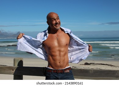 Bald Muscle Man Ripping Short Open With Ocean Backdrop