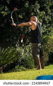 Bald Muscled Man Standing With Bow And Arrow Shooting