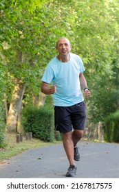 Bald Older Man Running Through The Park And Doing Sports To Get In Shape And Slim His Belly