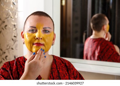 A Bald Woman Applies A Cosmetic Mask On Her Face In The Bathroom Near The Mirror. Horizontal Photo