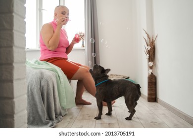 Bald woman is blowing bubbles with joy while spending time with her dog